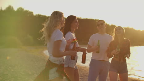 Group-of-students-celebrate-the-end-of-the-semester-with-beer-on-the-beach.-They-are-dancing-and-drinking-beer-on-the-open-air-party-at-sunset-in-summer-evening.